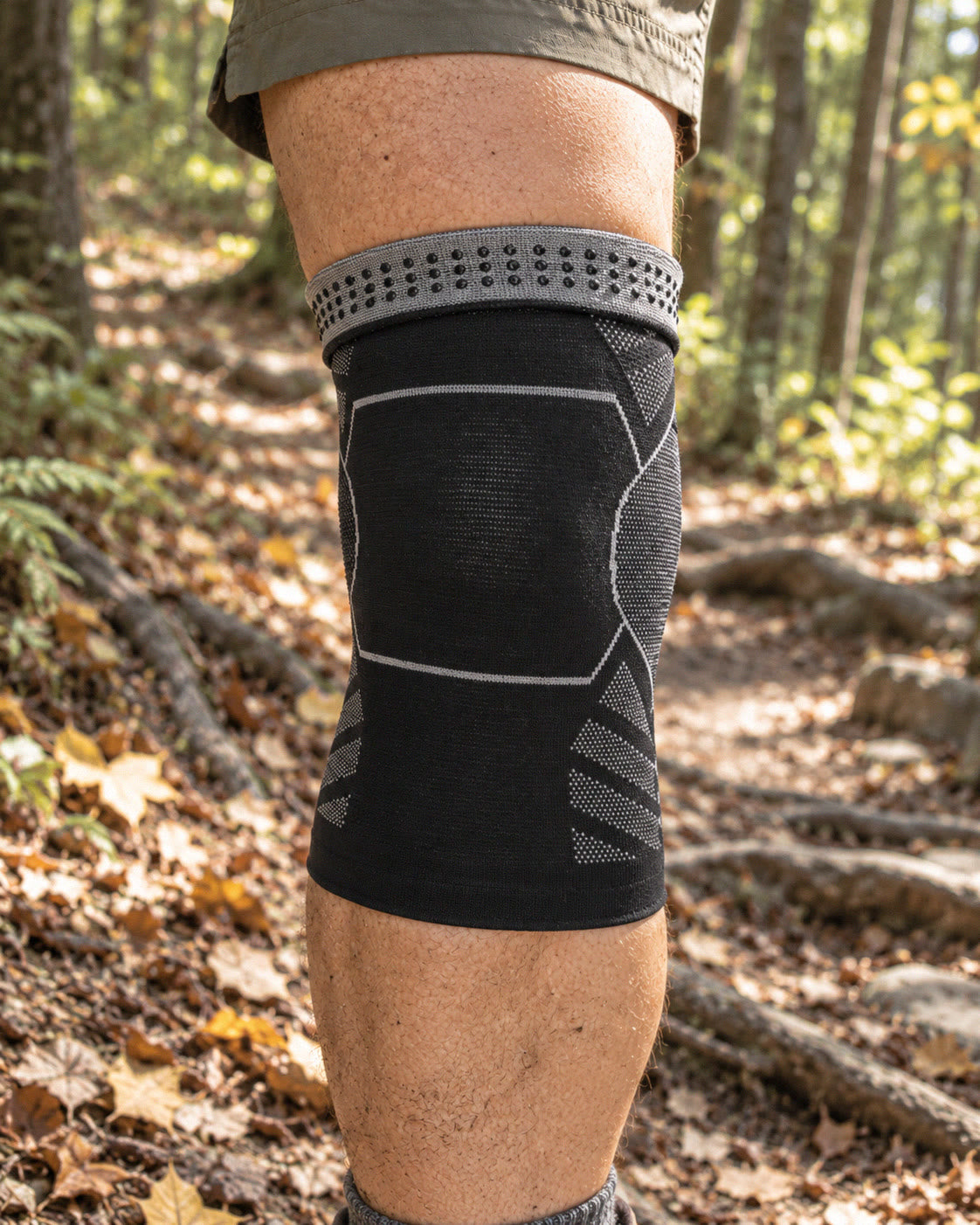 Knee sleeve on a hiker's knee on a forest trail, top folded down to show the grey band with silicone dots